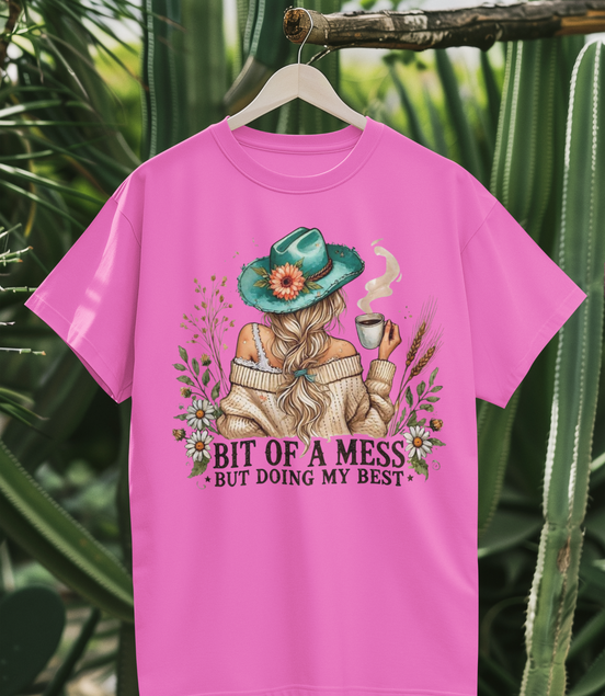 Pink t-shirt with a graphic design of a person in a hat and scarf, holding a cup, surrounded by plants.
