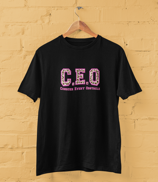 Black t-shirt with 'C.E.O. Conquer Every Obstacle' text on a yellow brick wall background