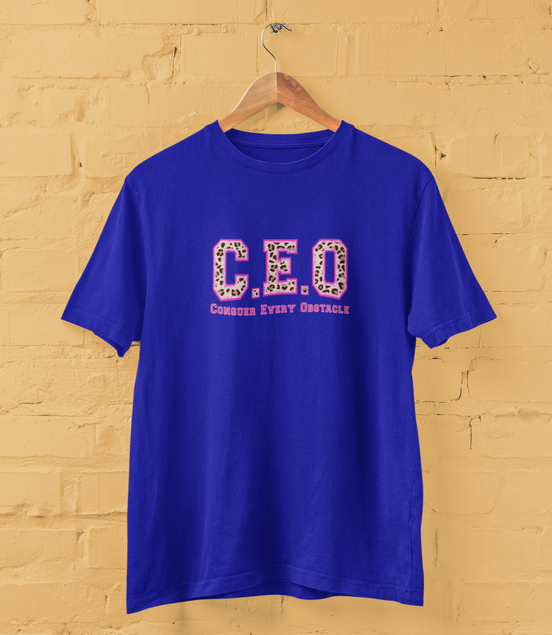 Blue t-shirt with 'CEO Conquer Every Obstacle' text on a yellow brick wall background