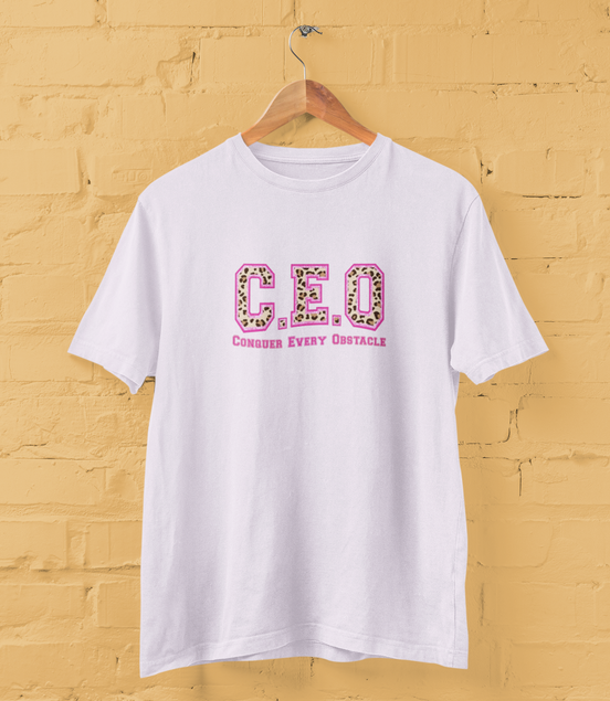 White t-shirt with 'C.E.O. Conquer Every Obstacle' text on a yellow brick wall background
