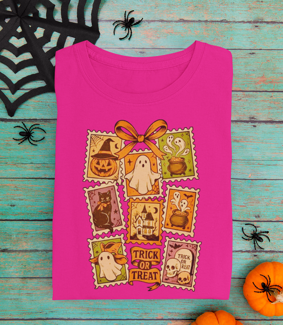 Pink t-shirt with Halloween-themed postage stamps design on a wooden surface.