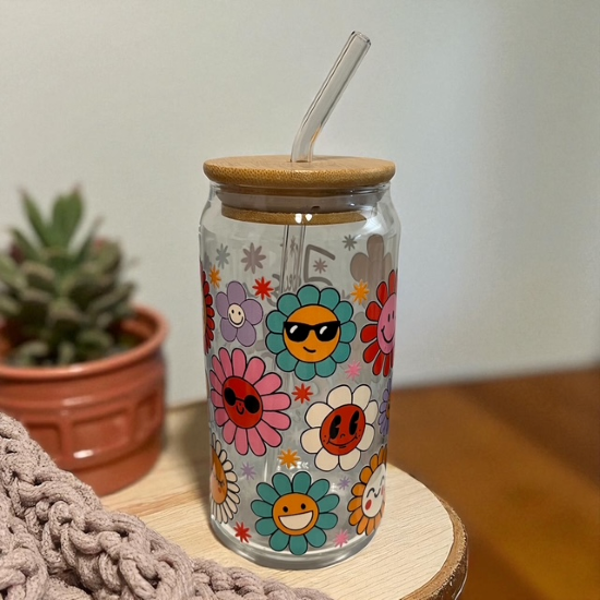 Glass tumbler with floral designs and a wooden lid on a wooden surface.