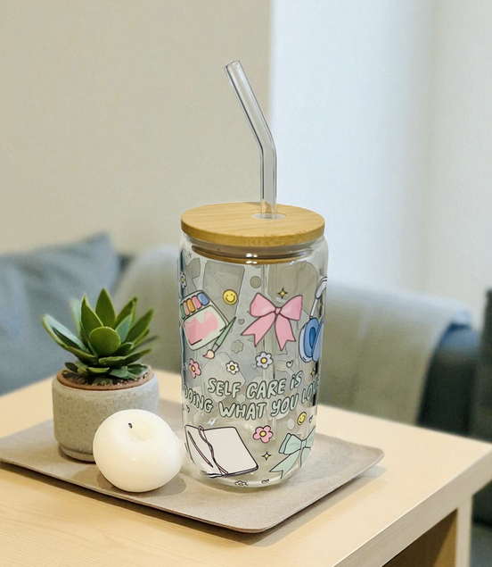 Glass tumbler with a wooden lid and straw on a table with a plant and candle.