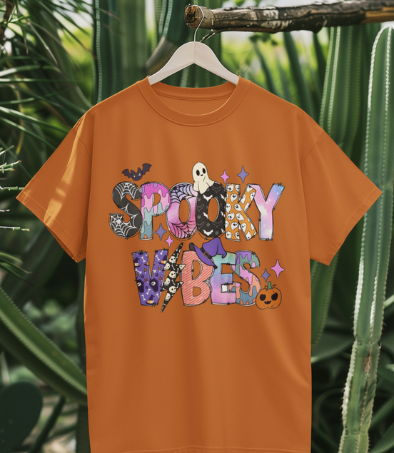 Orange t-shirt with 'Spooky Vibes' text and graphics on a hanger against a cactus background