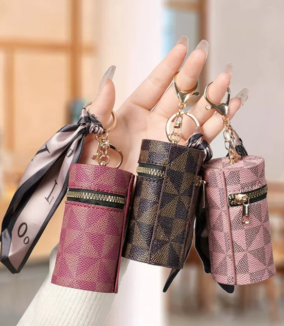 Three small handbags with keychains held by a hand against a blurred indoor background.