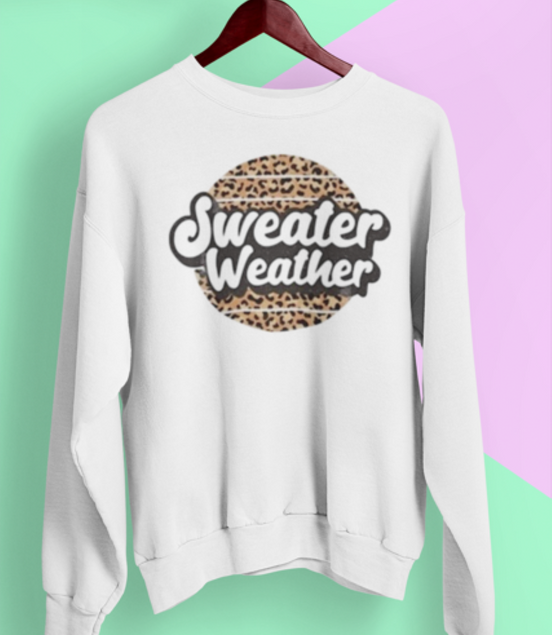 White sweatshirt with 'Sweater Weather' text and leopard print design on a hanger against a colorful background.