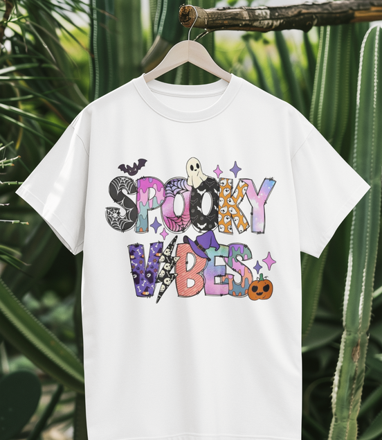 White t-shirt with colorful 'Spooky Vibes' text design on a hanger against a cactus background